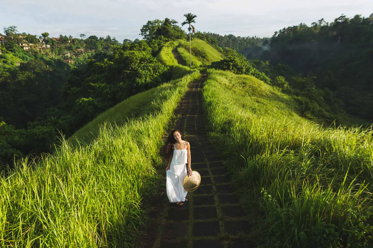 A woman walking a stone path between green rice terraces.